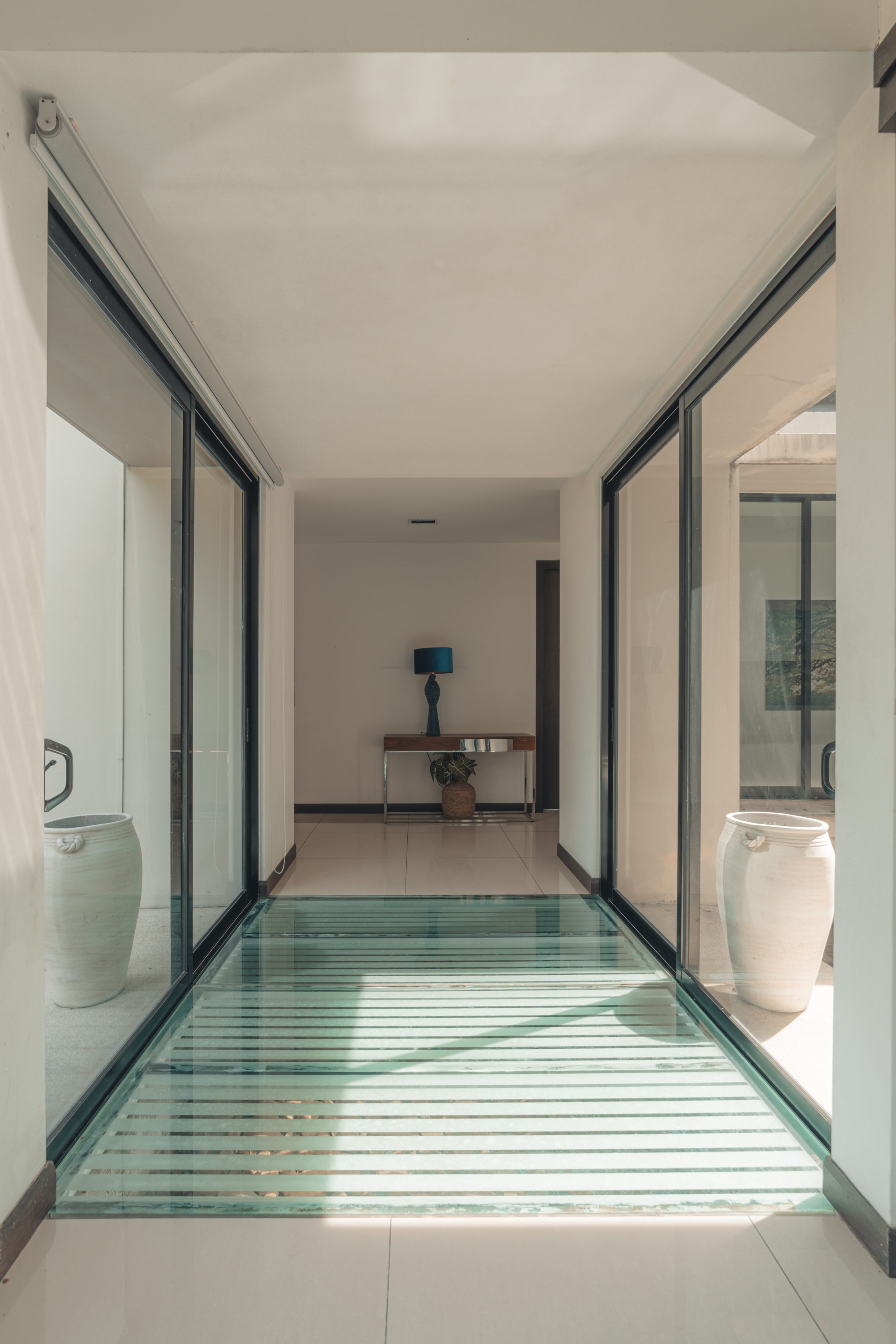 Narrow glazed passage crossing a shallow water court between white walls at Leisure Farm